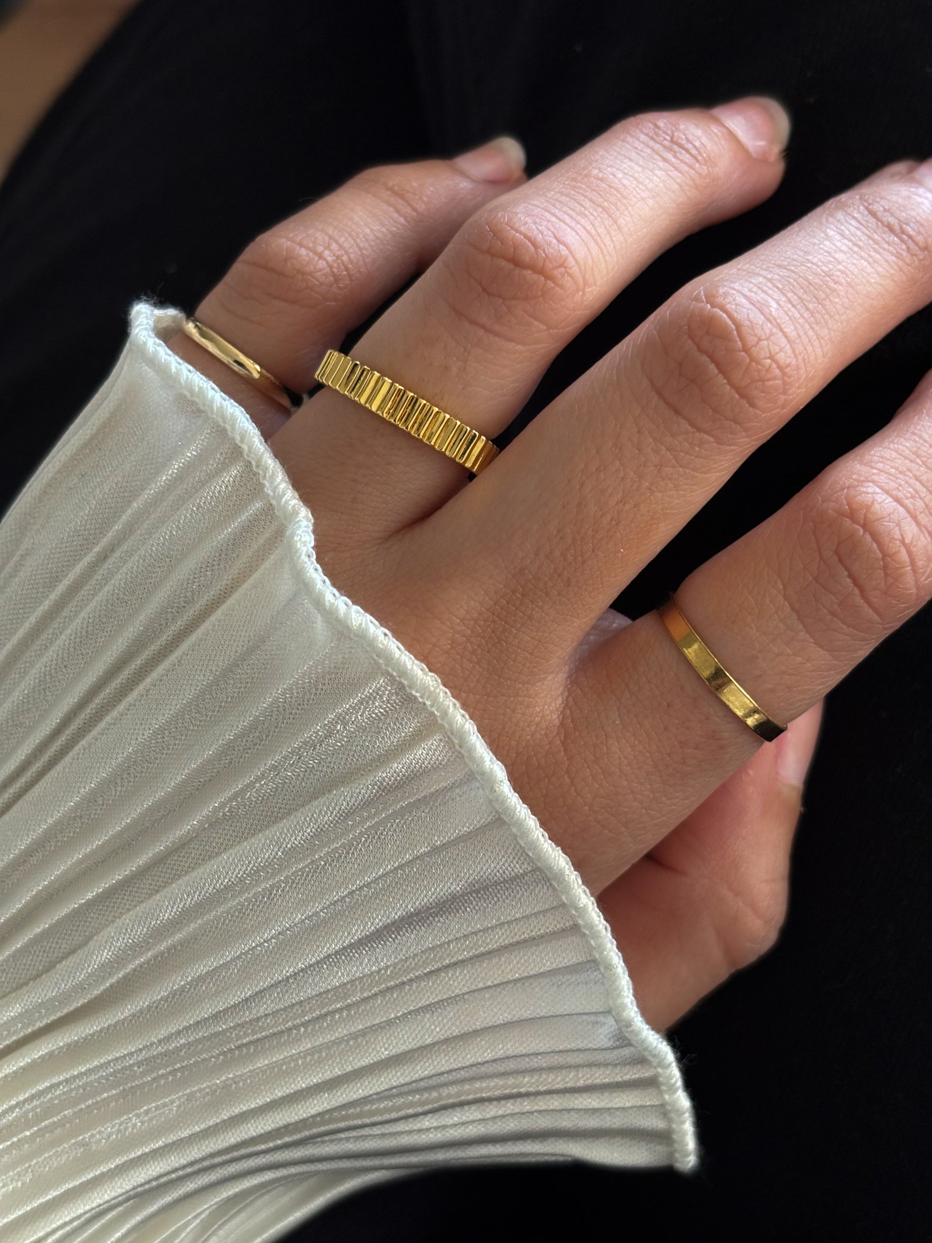 A simple gold band ring with grooved texture, displayed against a white background
