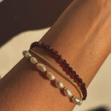 Bracelet with red and gold beads on a wrist against a neutral background