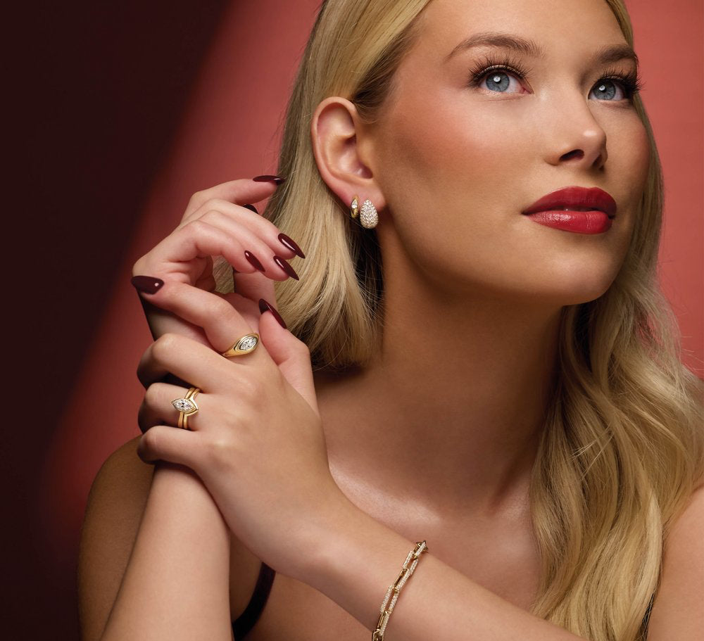Woman wearing 14K yellow gold diamond earrings and rings against a red background