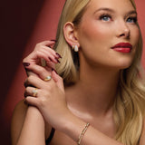 Woman wearing 14K yellow gold diamond earrings and rings against a red background