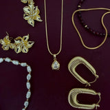 A flat-lay collection of gold and pearl jewelry on a dark burgundy background, including a gold pendant necklace, gold hoop earrings, gold flower earrings, a pearl bead bracelet, and a dark red beaded necklace.