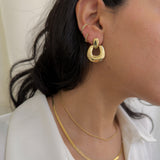 Close-up of a person wearing gold hoop earrings and necklaces against a neutral background